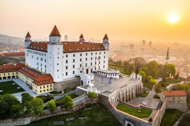 A historic castle overlooks Bratislava with the city skyline in the background at sunset, HD Desktop Wallpaper