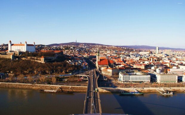 A panoramic view of Bratislava city with the Danube river and historic architecture under a clear sky, 2K Desktop Wallpaper
