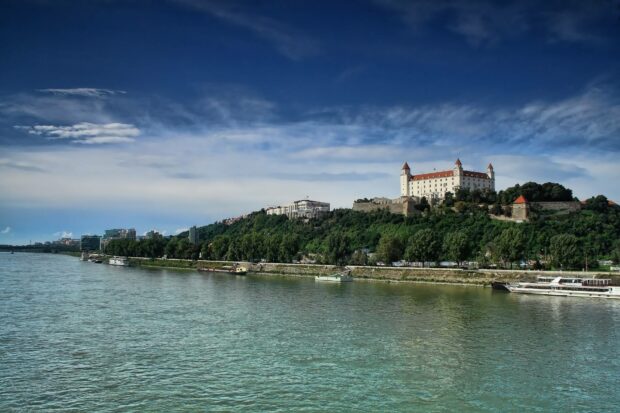 Bratislava Wallpapers showcase a panoramic view of the river and the historic castle atop a green hill, HD Desktop Wallpaper