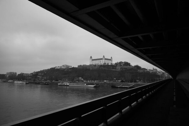 The Bratislava cityscape shows the historic castle on a hill with the Danube river and boats under an overcast sky, HD Desktop Wallpaper