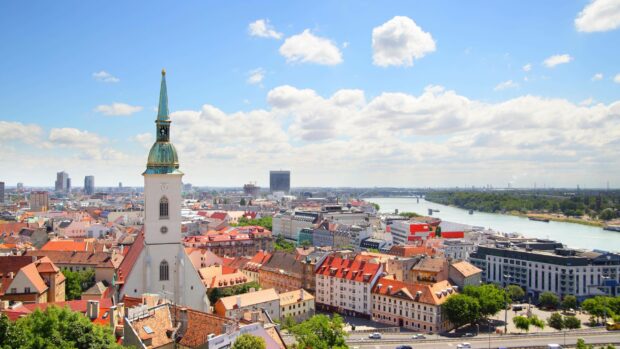 A panoramic view of Bratislava showing the old town, river, and city buildings under a cloudy sky, 2K Desktop Wallpaper