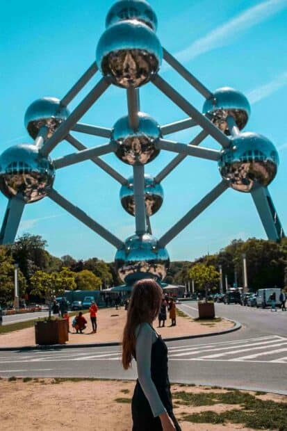 A woman is standing near the Atomium structure under a bright blue sky in Brussels, HD Mobile Wallpaper