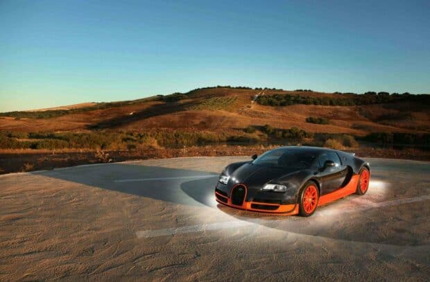 A Bugatti Veyron car with black and orange details is parked on a helipad in a dry landscape under a clear sky, 2K Desktop Wallpaper