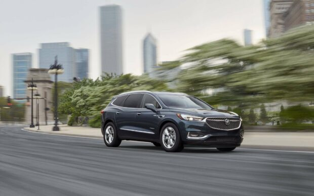 A Buick Enclave is driving on a city street with trees and tall buildings in the background, 2K Desktop Wallpaper