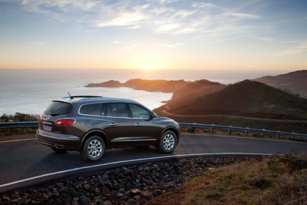 A Buick Enclave driving along a winding coastal road at sunset with ocean and hills in the background, 2K Desktop Wallpaper