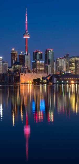 The CN Tower Canada stands brightly lit against the clear night sky with its reflection in the water, 2K Phone Wallpaper