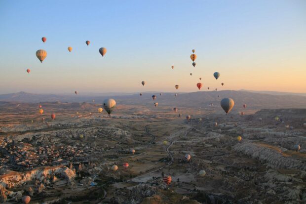A scenic view of Cappadocia with numerous hot air balloons floating over the rocky landscape during sunrise, 2K Desktop Wallpaper