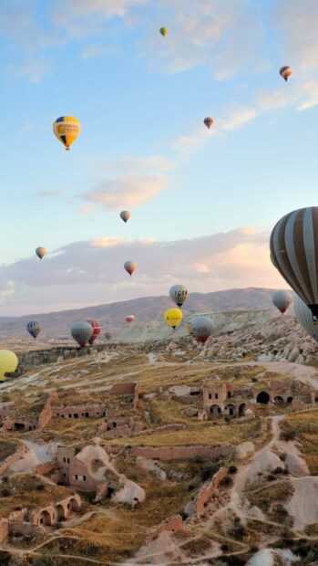 Hot air balloons fly over historical rock formations in Cappadocia at sunrise, HD Phone Wallpaper