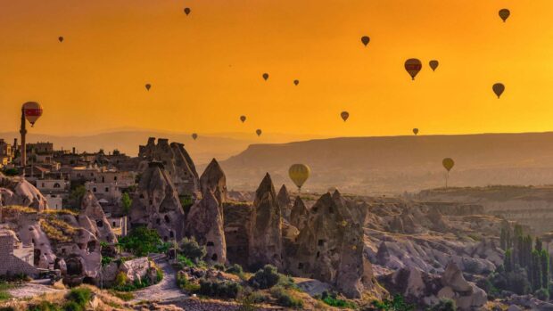 The sky is filled with hot air balloons floating above Cappadocia's unique rock formations at sunset, HD Desktop Wallpaper