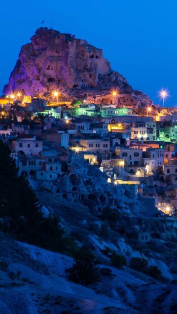 The night view shows Cappadocia town with rock formations and lit houses under a clear blue sky, HD Mobile Wallpaper