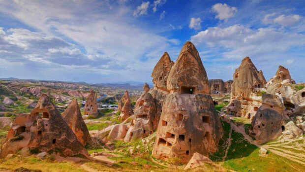 The Cappadocia rock formations stand tall under a partly cloudy blue sky with green patches around, HD Desktop Wallpaper