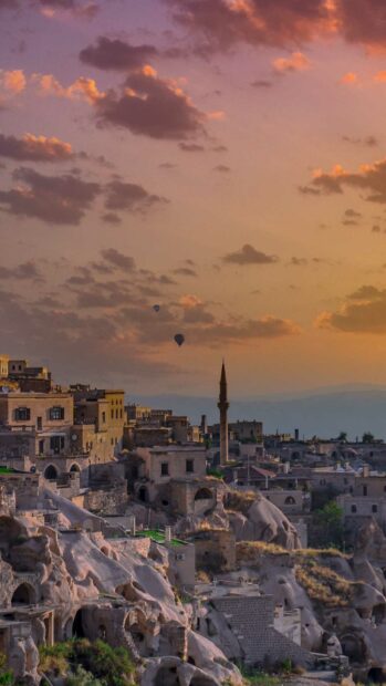 The sun sets over Cappadocia with rocky dwellings and a vibrant sky featuring two hot air balloons, HD Mobile Wallpaper