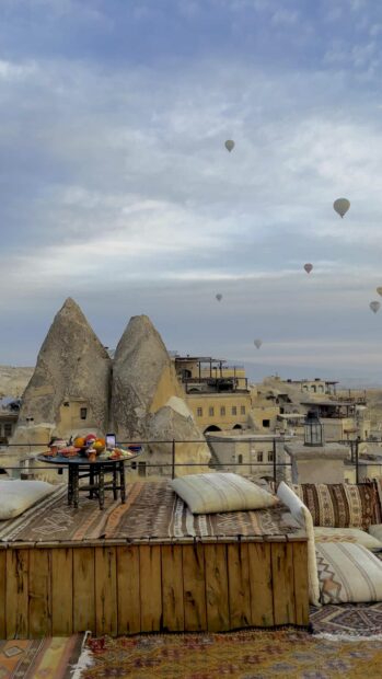 A serene view of Cappadocia with hot air balloons floating over rock formations and traditional seating, 4K Phone Wallpaper