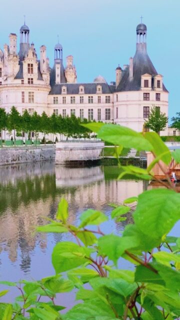 Chateau De Chambord Reflecting On Calm Water With Greenery In Foreground Wallpaper