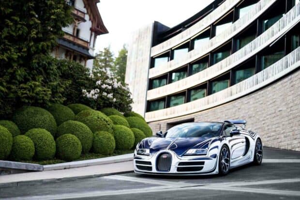 A chrome Bugatti Veyron is parked on a road beside a modern building with green bushes nearby, 2K Desktop Wallpaper