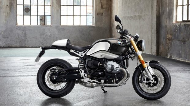 A black and white BMW R Nine T motorcycle stands inside an industrial garage with large windows, 4K Desktop Wallpaper