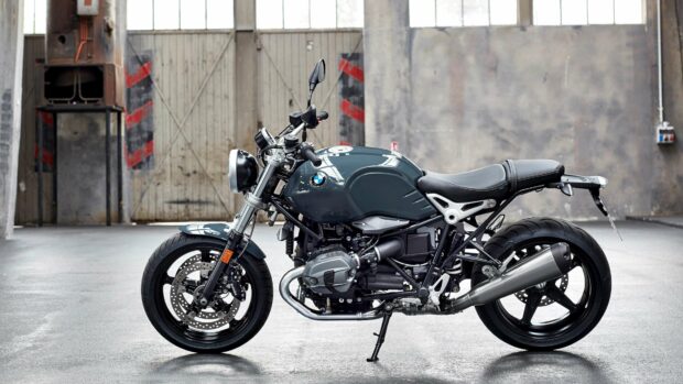 A BMW R Nine T motorcycle is parked in an industrial garage with a concrete floor and weathered walls, 4K Desktop Wallpaper