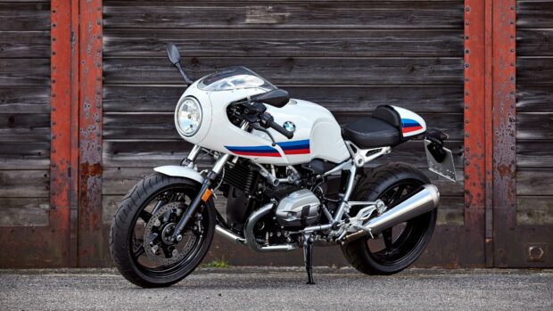 A white BMW R Nine T motorcycle is parked in front of a wooden wall with rusty metal beams, 4K Desktop Wallpaper