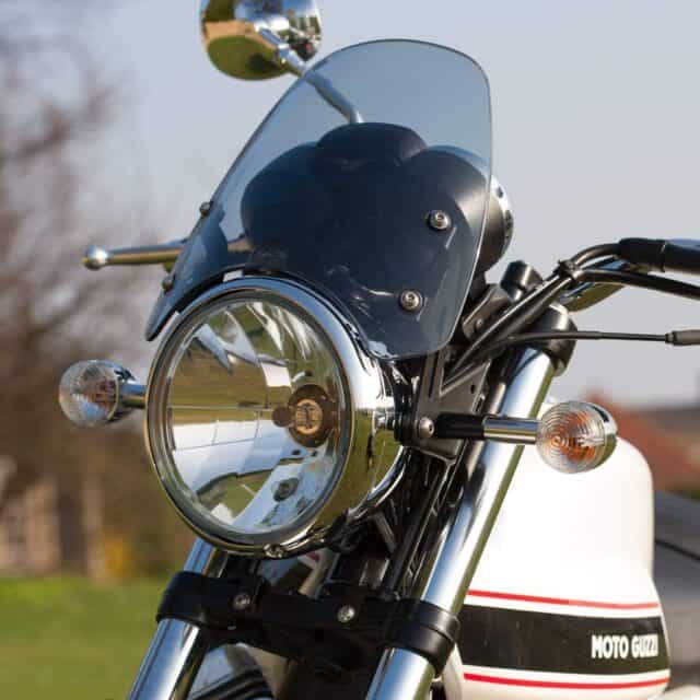 Close up view of Moto Guzzi V7 motorcycle front headlight and windscreen in outdoor setting wallpaper