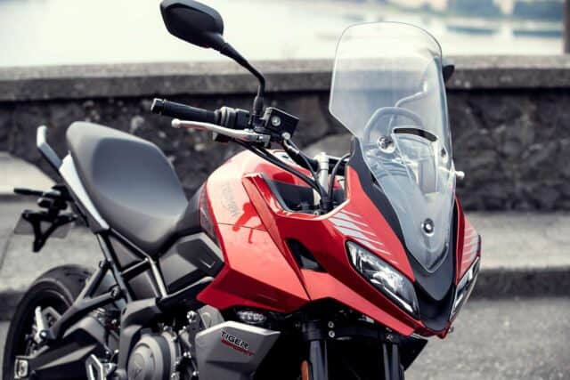 Close up view of red Triumph Tiger Sport 660 motorcycle parked by stone wall wallpaper