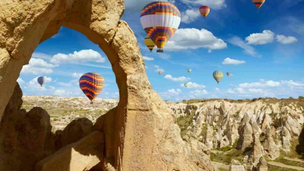 The colorful hot air balloons float over the rocky formations of Cappadocia under a bright blue sky, HD Desktop Wallpaper