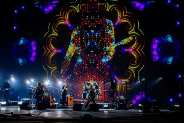 A live band is performing on stage with vibrant and colorful light projections behind them during a concert, 2K Desktop Wallpaper