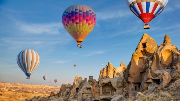 A vibrant scene with hot air balloons flying above the unique rock formations in Cappadocia captured during sunrise, HD Desktop Wallpape