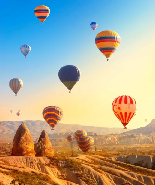 A group of colorful hot air balloons is flying over the rocky terrain of Cappadocia during sunrise, HD Mobile Wallpaper