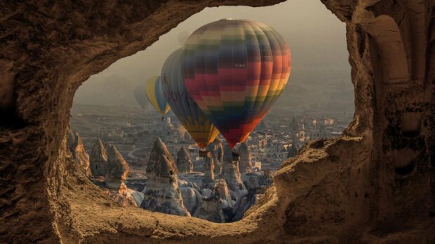 The colorful hot air balloons in Cappadocia float above unique rock formations framed by a cave opening, capturing a stunning landscape view, HD Desktop W