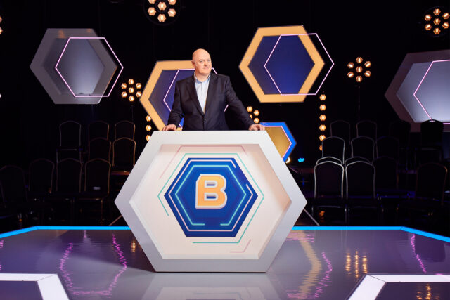 Dara Ó Briain Hosting Game Show On Stage Hexagonal Design Backdrop