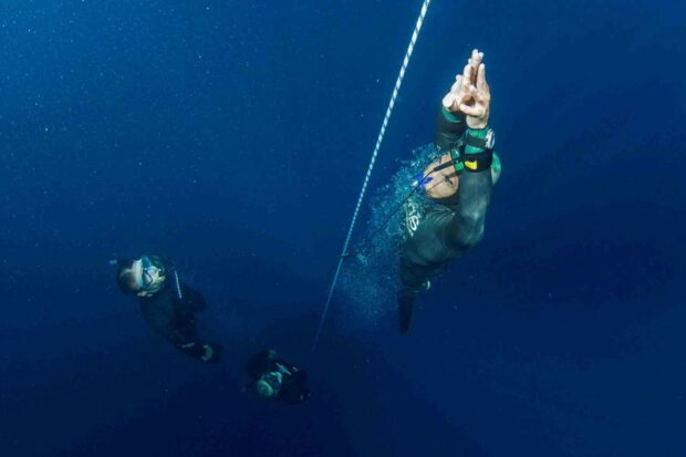 A freediver descends along a rope underwater with two others in deep blue sea, 2K Desktop Wallpaper