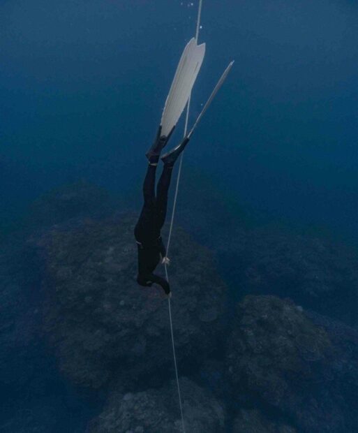 A freediver descends underwater holding a rope with fins in the deep ocean, HD Mobile Wallpaper
