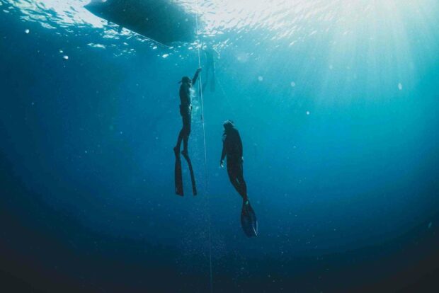 Two freedivers exploring underwater with calm sun rays illuminating them, HD Desktop Wallpaper