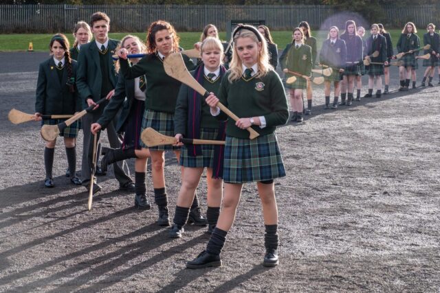 Derry Girls TV Series Cast in School Uniforms Holding Hurling Sticks Outdoor Wallpaper