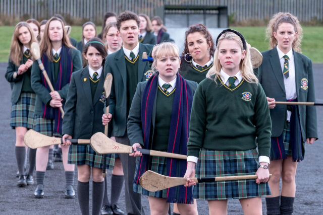 Derry Girls TV Series Group Photo with School Uniforms and Hurling Sticks Wallpaper