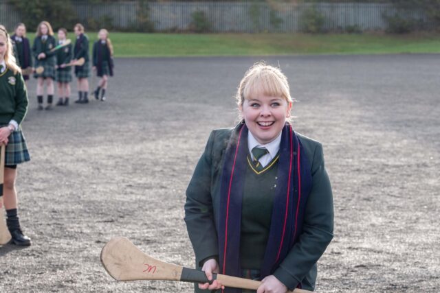 Derry Girls TV Series Wallpaper Erin Holding Hurling Stick on School Playground