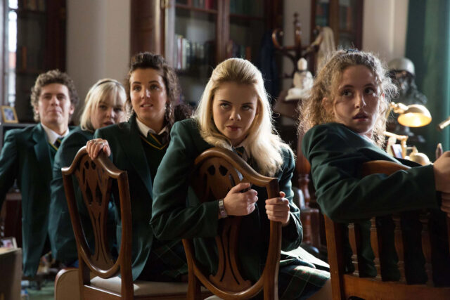Derry Girls TV Series Wallpaper Group of Students in Uniform Sitting on Chairs in Classroom