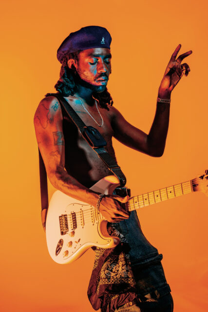 Dev Hynes Guitar Performance Vivid Orange Background Wallpaper