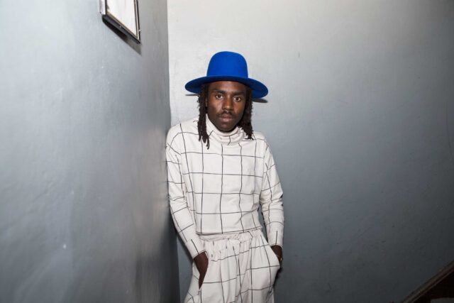 Dev Hynes Stylish Portrait In Blue Hat And Grid Outfit Wallpaper