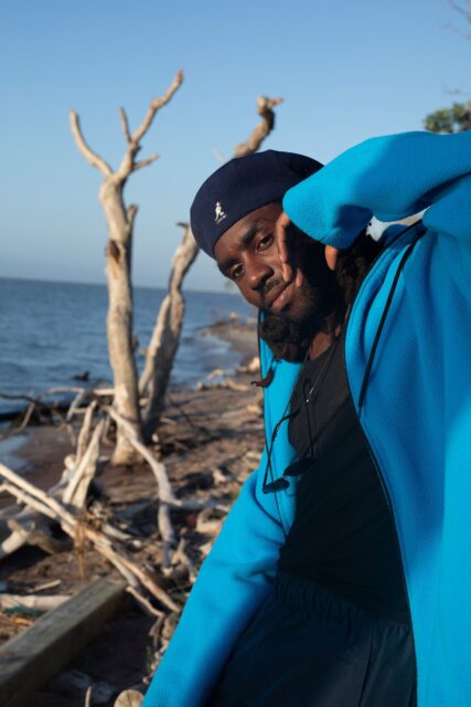Dev Hynes By The Beach In Blue Hoodie Wallpaper