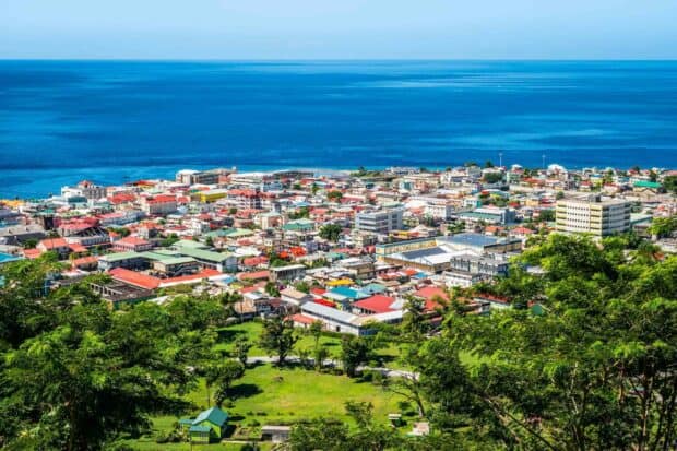 A scenic view of a Dominica town near the deep blue sea surrounded by green foliage, 2K Desktop Wallpaper