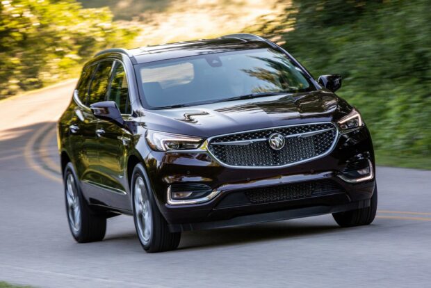 A black Buick Enclave is driving on a curved road surrounded by green trees and sunlight, 2K Desktop Wallpaper