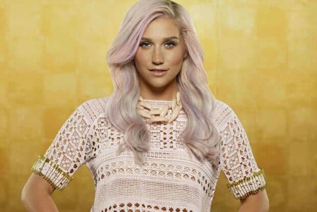 A portrait of Kesha wearing a detailed crochet top and beige necklace with pastel pink hair against a golden background, HD Desktop Wallpaper