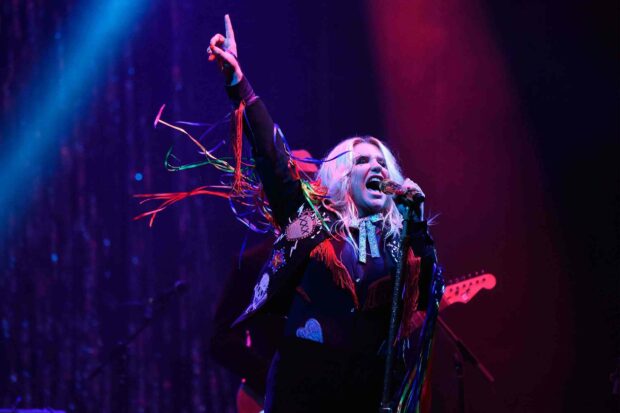 Kesha is passionately singing and raising her hand during a colorful live concert, 2K Desktop Wallpaper