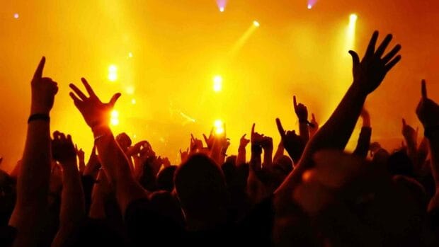 A lively concert crowd raising their hands under bright yellow stage lights, HD Desktop Wallpaper