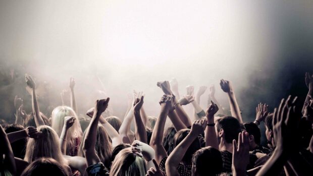 A large crowd with raised hands enjoying a concert in a smoky venue, 4K Desktop Wallpaper