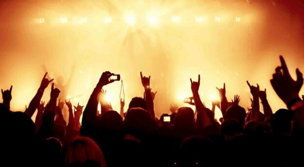 An excited crowd is raising hands and capturing moments during a concert with bright stage lights in the background