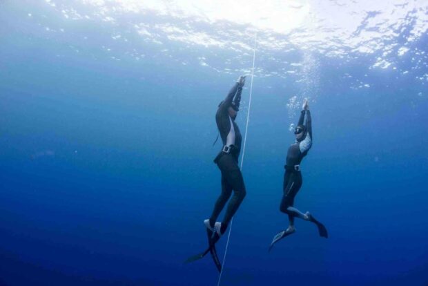 Two freediving athletes descend underwater alongside a guide line in the deep blue ocean, HD Desktop Wallpaper