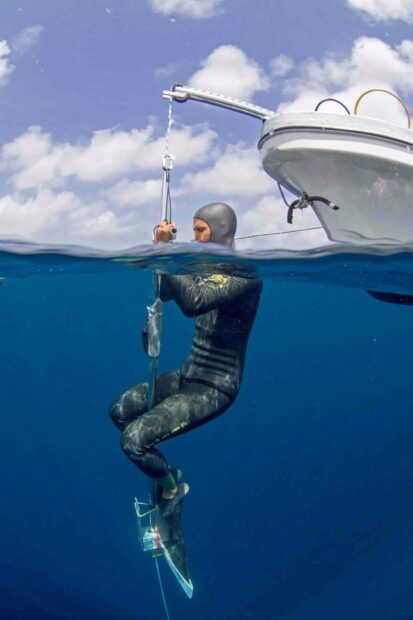 A freediver is preparing to descend into deep blue water holding a dive line near a boat, 2K Mobile Wallpaper