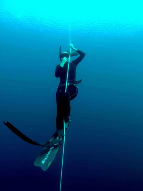 A freediver wearing fins and a wetsuit descends holding a rope in the deep blue ocean, 2K Desktop Wallpaper